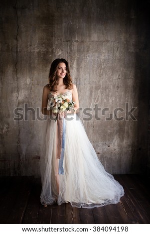 beige bride in a wedding dress holding a bouquet of anemones on a background of textured walls in the loft Royalty-Free Stock Photo #384094198