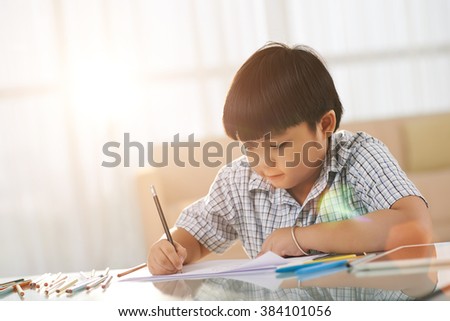 Vietnamese little boy sitting at table and drawing pictures