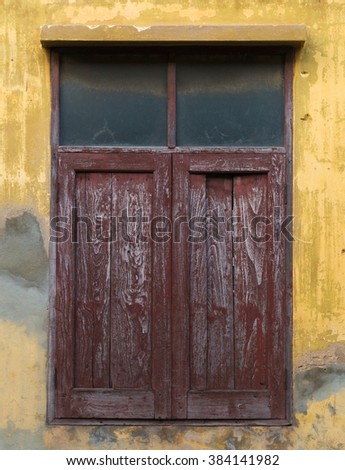 Old wooden window on yellow weathered wall