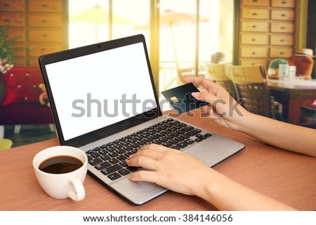 laptop and hand holding credit card with blur image of people in coffee shop