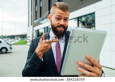 Young bearded businessman using his tablet pc. He is surprised. Outdoor photo