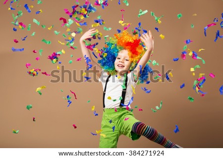 Little boy in clown wig jumping and having fun celebrating birthday. Brazilian Carnival. Venice Carnival. child throws up a multi-colored tinsel and confetti. Birthday boy. Positive emotions.  Royalty-Free Stock Photo #384271924