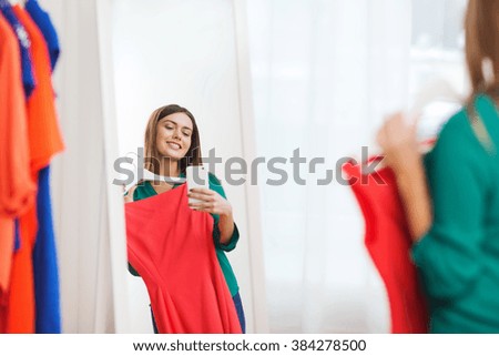 clothing, fashion, style, technology and people concept - happy woman with smartphone snd red dress taking mirror selfie at home wardrobe