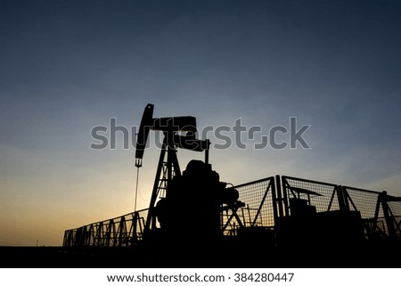 Silhouette of crude oil pump at sunset in oilfield.