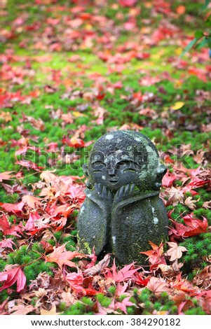 Colorful red maple leaves fallen on the ground with green grass and beautiful rock doll Jizo (little Japanese Buddha monk statue) in autumn season. Kyoto, Japan. Travel and holiday vacation concept.