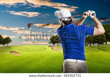 Golf Player in a blue shirt taking a swing, on a golf course.
