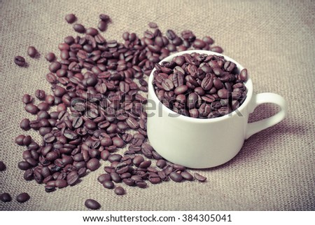 Cup, saucer and coffee beans on a burlap background. Selective focus. Toned.