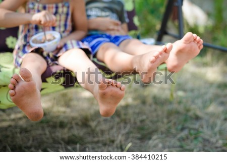 Closeup of happy kids sitting and swing on sunny countryside background. Picture of two children legs barefoot. 