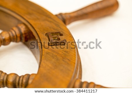 Wooden letter E on  vintage wooden ship steering wheel, close up 