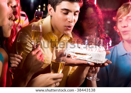 Man with his friends blow out candle on cake at birthday