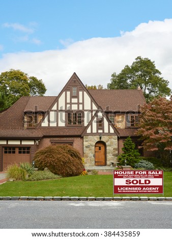 Real estate sold (another success let us help you buy sell your next home) sign Beautiful Tudor Style Suburban Home Residential Neighborhood Blue Sky Clouds USA