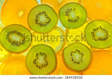 Fresh slices of lemon, orange and kiwi sliced by circles and lying in the water with bubbles