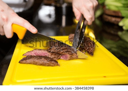 Cutting flame grilled, cooked kangaroo steak loin on a yellow cutting board