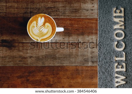 cup of latte art coffee on wooden background with sign welcome