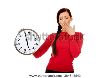 Young yawning woman holding a clock