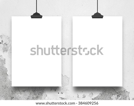 Close-up of two hanged paper sheet frames with clips on light grey weathered wall background