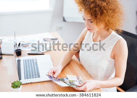 Cute lovely redhead young woman photographer sitting on workplace and choosing photos