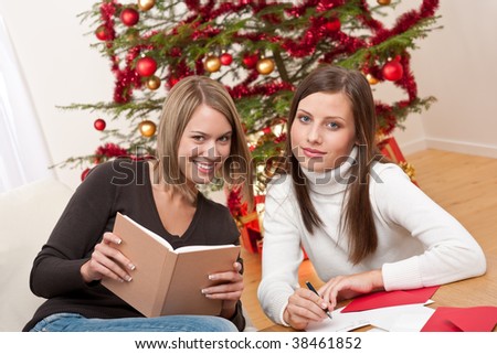 Two young women writing Christmas cards in front of tree
