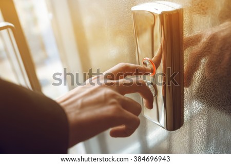 finger presses the elevator button. Red button. sunset light. businessman is a lift. high floor. hand reaches for the button of the elevator call. Royalty-Free Stock Photo #384696943