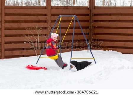 little girl with a dog riding on a swing in the snow