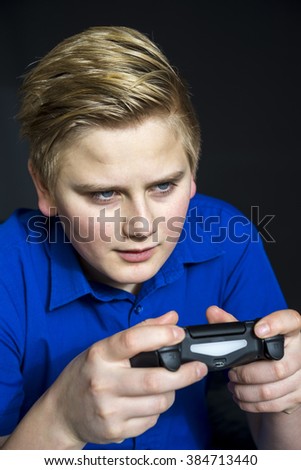 Serious young male teen in blond hair and blue shirt hunched over while holding video game controller with serious expression