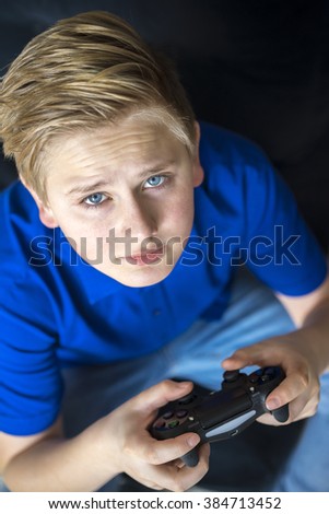 Serious single male teenager in blue shirt and eyes playing video games with controller while looking up