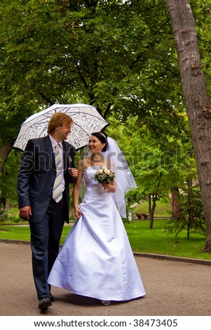 newlyweds with umbrella walk in park