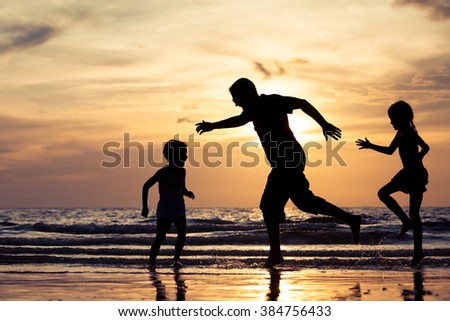 Father and children playing on the beach at the sunset time. Concept of happy friendly family.
