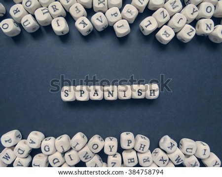 Word Spanish of small white cubes next to a bunch of other letters on the surface of the composition on a dark background                                