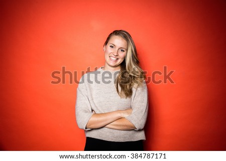 Smiling Blonde woman with grey wool jersey posing in front of orange background in studio with vibrant contrasty light