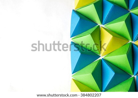 Creative background with blue, green and yellow origami tetrahedrons with free copy space on the left side. Great for using in web.