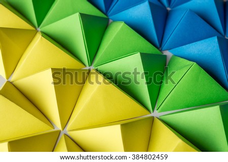 Creative background with blue, green and yellow origami tetrahedrons with free copy space on the left side. Great for using in web.