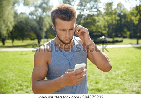 fitness, sport, technology and lifestyle concept - young man with smartphone and earphones listening to music at summer park