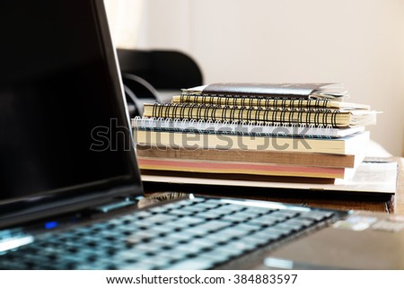 Pile of books and paperwork with blurred laptop, selective focus, shallow depth of field