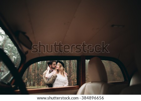 Gorgeous newlywed bride and groom posing in pine forest near retro car