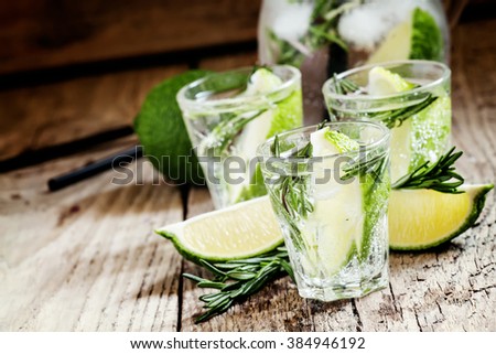 Drink with lime, rosemary, honey and soda, pitcher with crushed ice on the old wooden background, selective focus