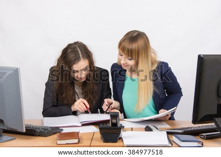 Two girls are looking for colleagues sitting together the right information at the same table in the office