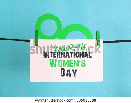 figure 8, paper flowers hang on clothespins in front of yellow background. International Women's Day. March 8, Happy Women's Day greeting message text