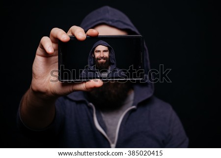 Hipster man with a beard taking picture smartphone self-portrait, screen view, snapshot studio on a black background