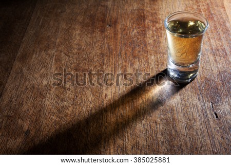 A shot glass of Brazilian gold cachaca isolated on rustic wooden background with beautiful shadow.