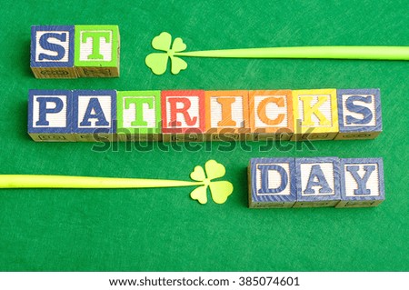St Patrick's day spelled with colorful alphabet blocks displayed with two four leaf clovers on a green background