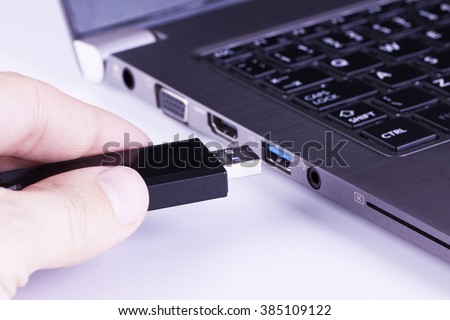 Black removable flash disk memory in fingers with laptop USB slot on white background Royalty-Free Stock Photo #385109122