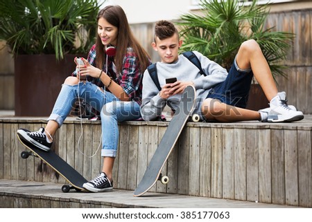 Girl and boy teens playing on mobile phones and listening to music outdoors