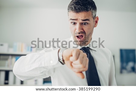 Stressed anxious businessman in a hurry checking time, he is late for his business appointment Royalty-Free Stock Photo #385199290