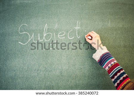 Hand with a piece of chalk writing message on a blackboard: Subject