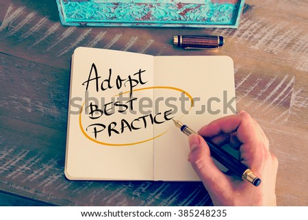 Retro effect and toned image of a woman hand writing a note with a fountain pen on a notebook. Handwritten text Adopt Best Practice as business concept image Royalty-Free Stock Photo #385248235