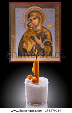 Burning candle before the icon of the Virgin Mary and Jesus in the background. Focus on the flame