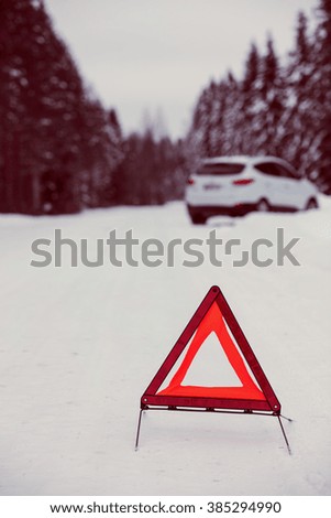 The red warning triangle laid out the road to warn of the accident in Finland. Focal point is a warning triangle. White car and the background out of focus. Image includes a vintage effect.