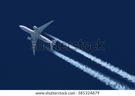 Civil wide-body airliner flying on a high altitude with condensation trail forming behind. Royalty-Free Stock Photo #385324879