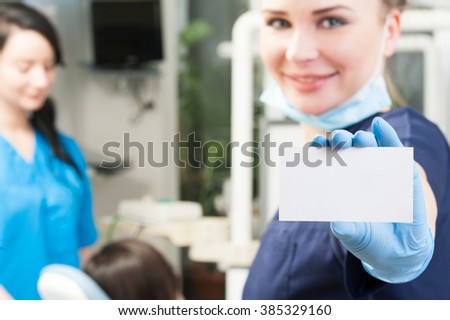 Woman dentist holding a blank white business card with copyspace in her dental office